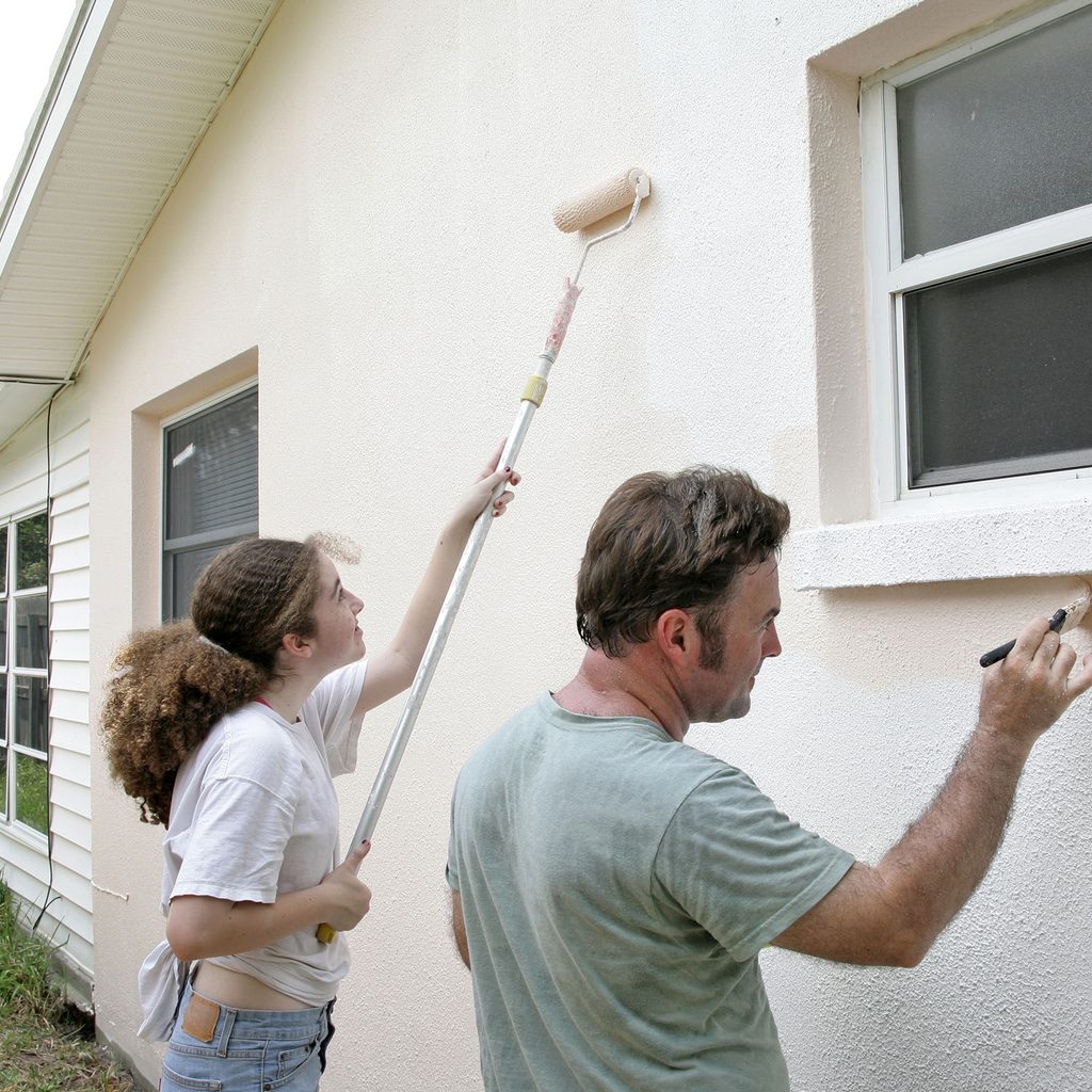 Father and daughter painting exterior of house