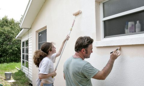 Father and daughter painting exterior of house