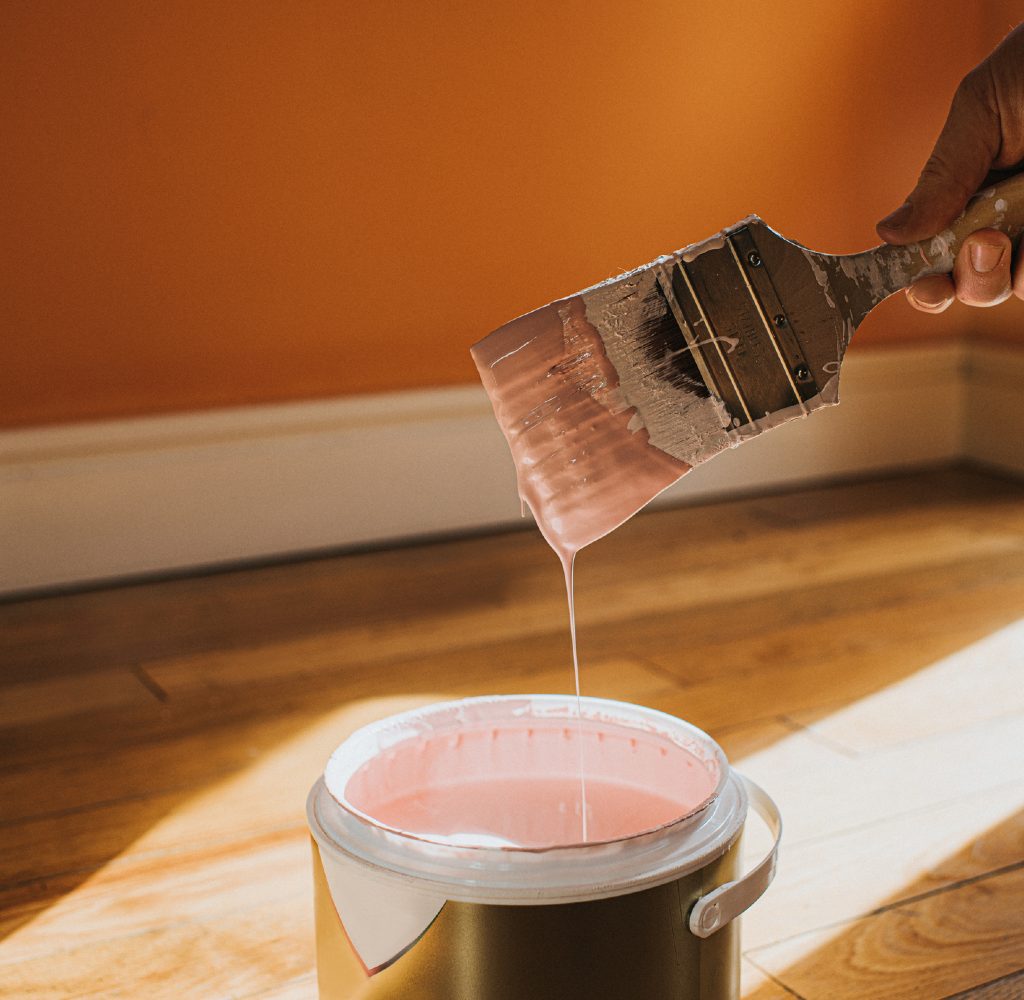 Hand holding paint brush over paint can.