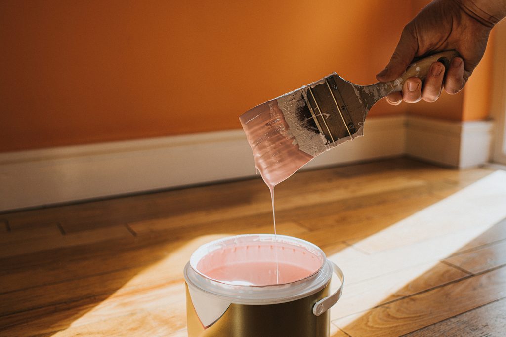 Hand holding paint brush over paint can.