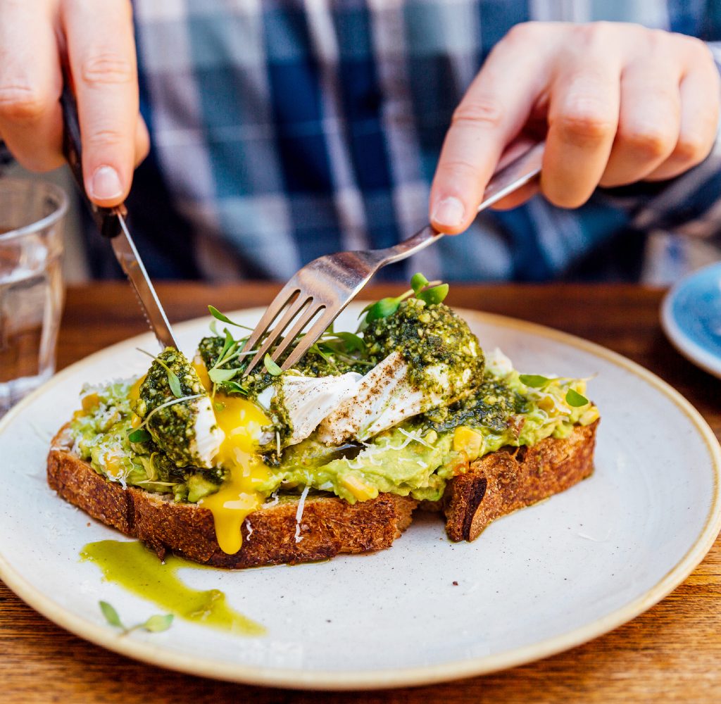 Man cutting into avocado toast with egg