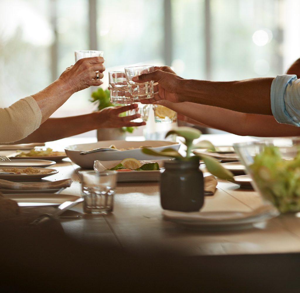 People toasting glasses at dining room table.