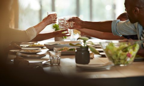 People toasting glasses at dining room table.