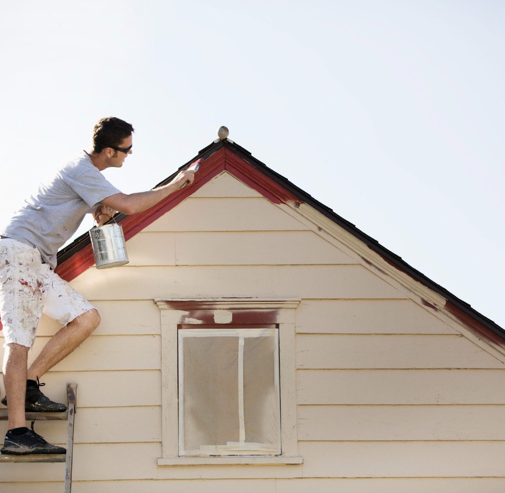 Guy on ladder painting exterior of house.