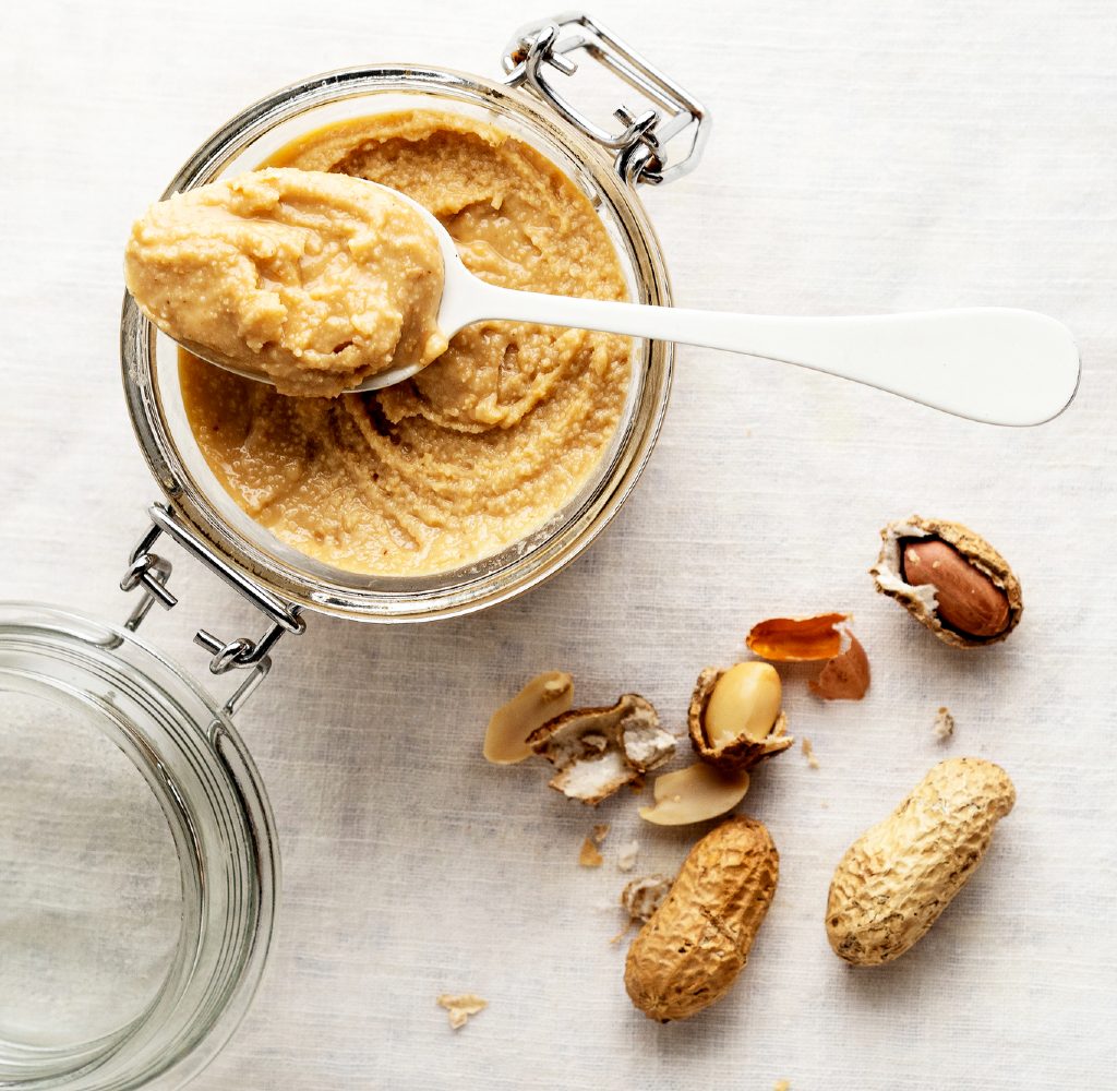 Homemade peanut butter in jar with peanuts next to it.