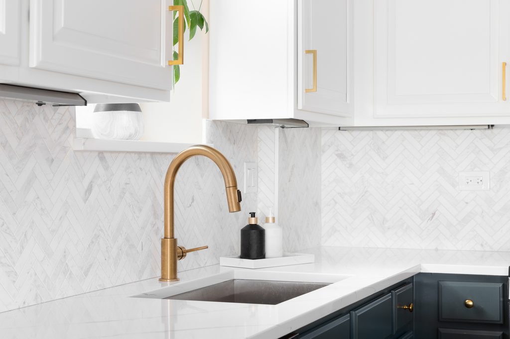 Gold kitchen sink faucet with herringbone backsplash and marble countertop