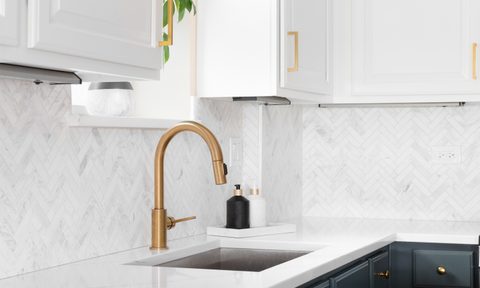 Gold kitchen sink faucet with herringbone backsplash and marble countertop