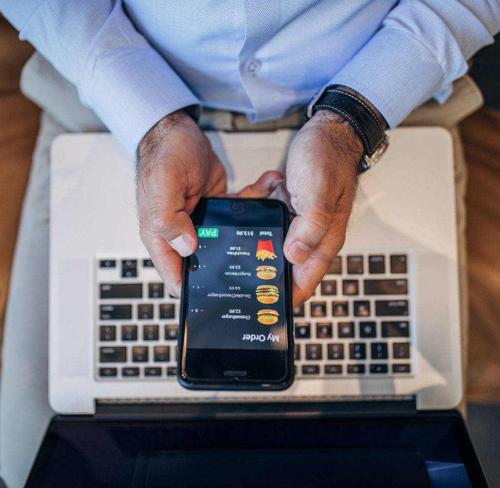 Person using fast food delivery app on phone with laptop on lap.
