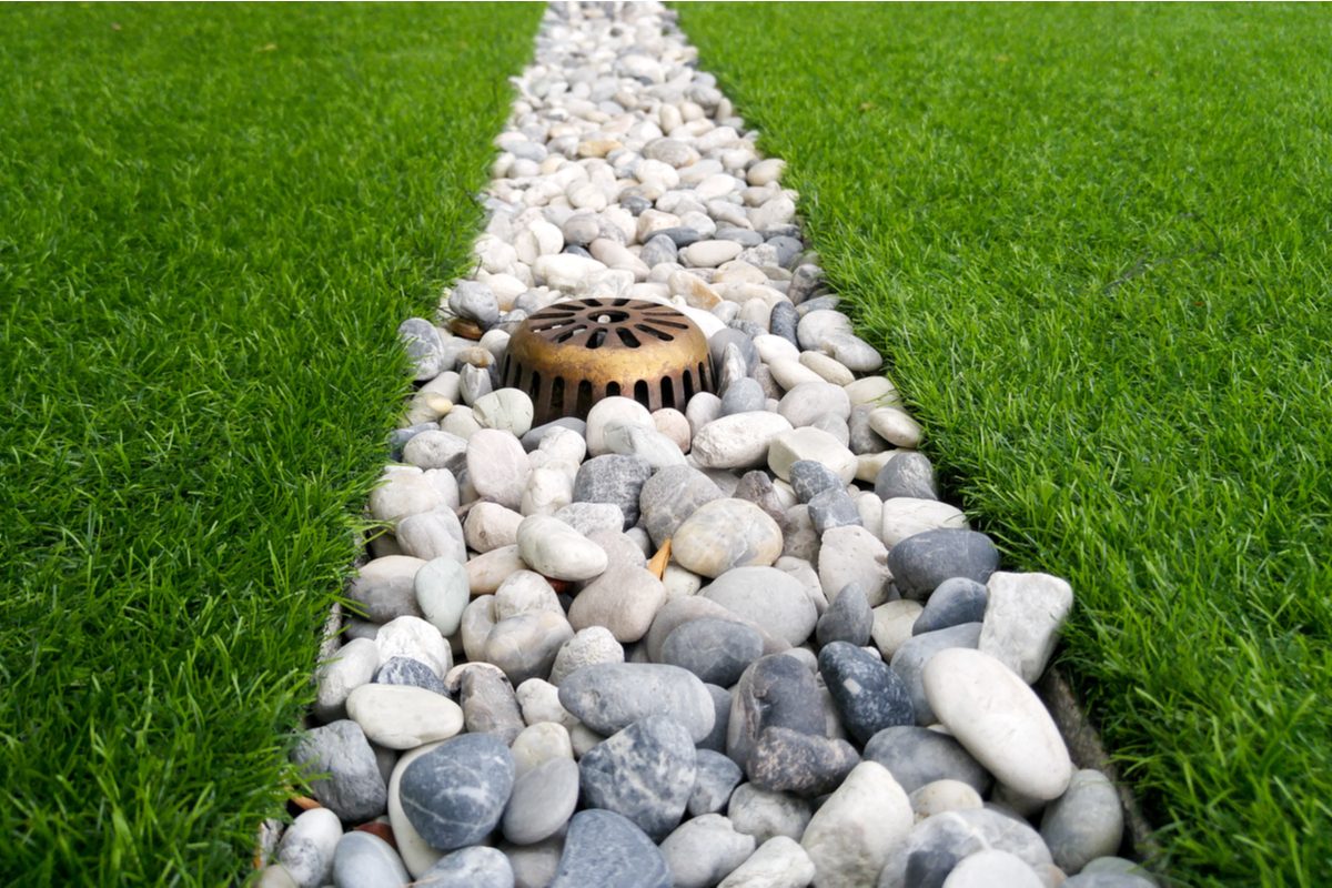 A French drain with white and gray rocks surrounded by green grass