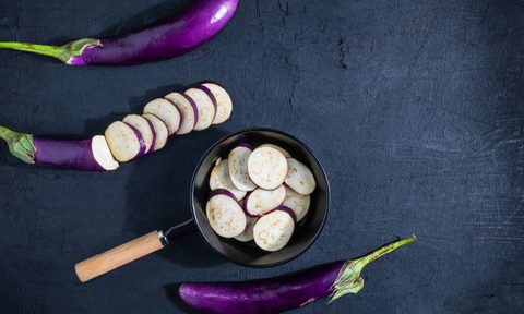 Sliced eggplant in a pot next to whole eggplants.
