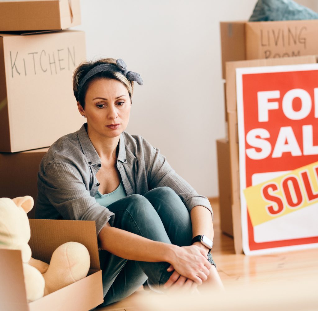 Woman looking sad with for sale sign.