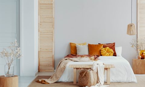 Brown and orange pillows on a white bed in natural bedroom interior with wicker lamp and wooden bedside table with vase