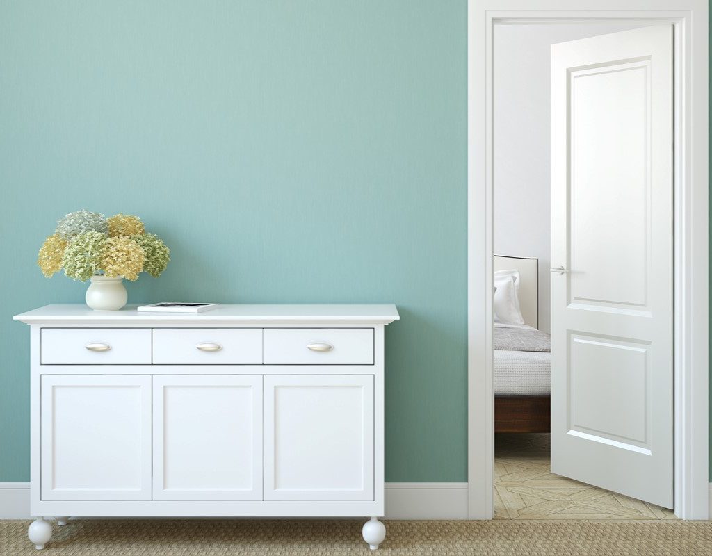 Light blue wall with white bedroom door, trim, and console table