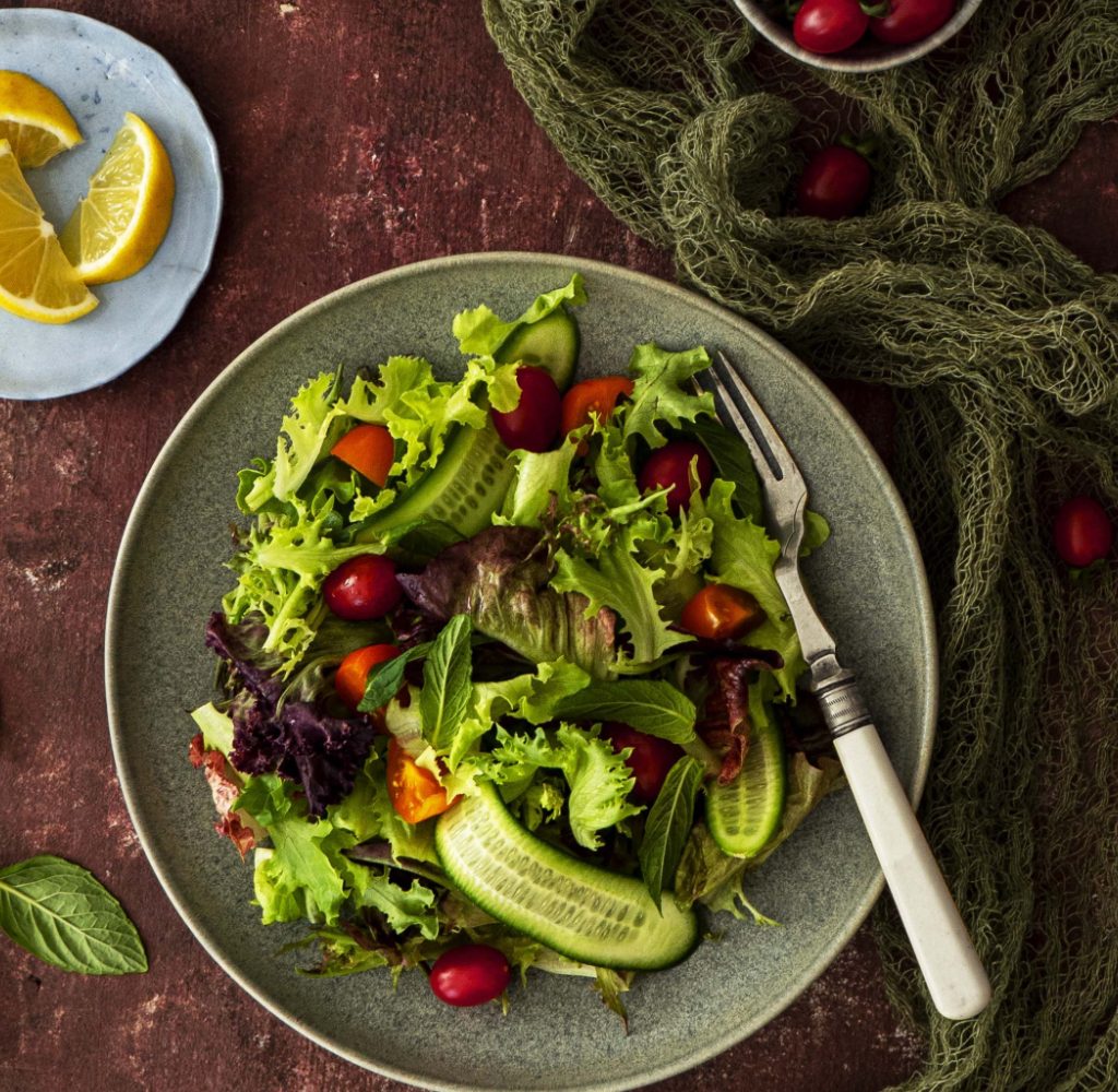 Mixed greens salad on table with small bowl of cut lemons.