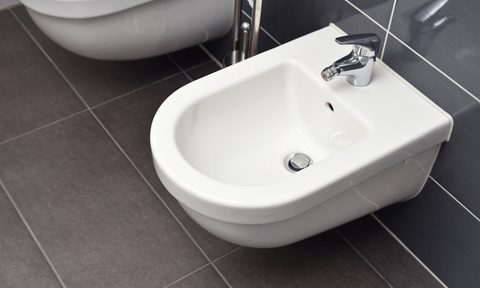 White bidet screwed to a gray-tiled wall