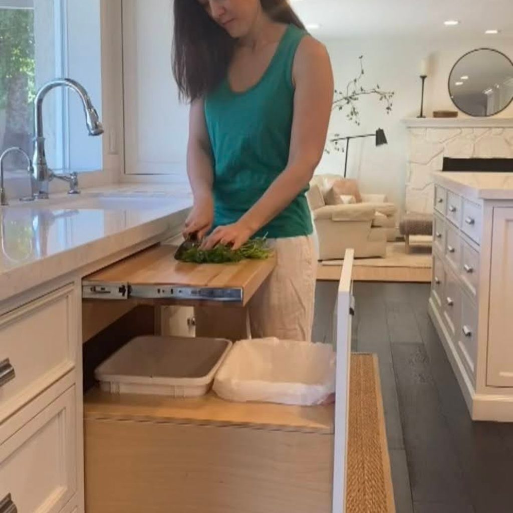 Woman cutting vegetables on pull-out cabinet cutting board in kitchen
