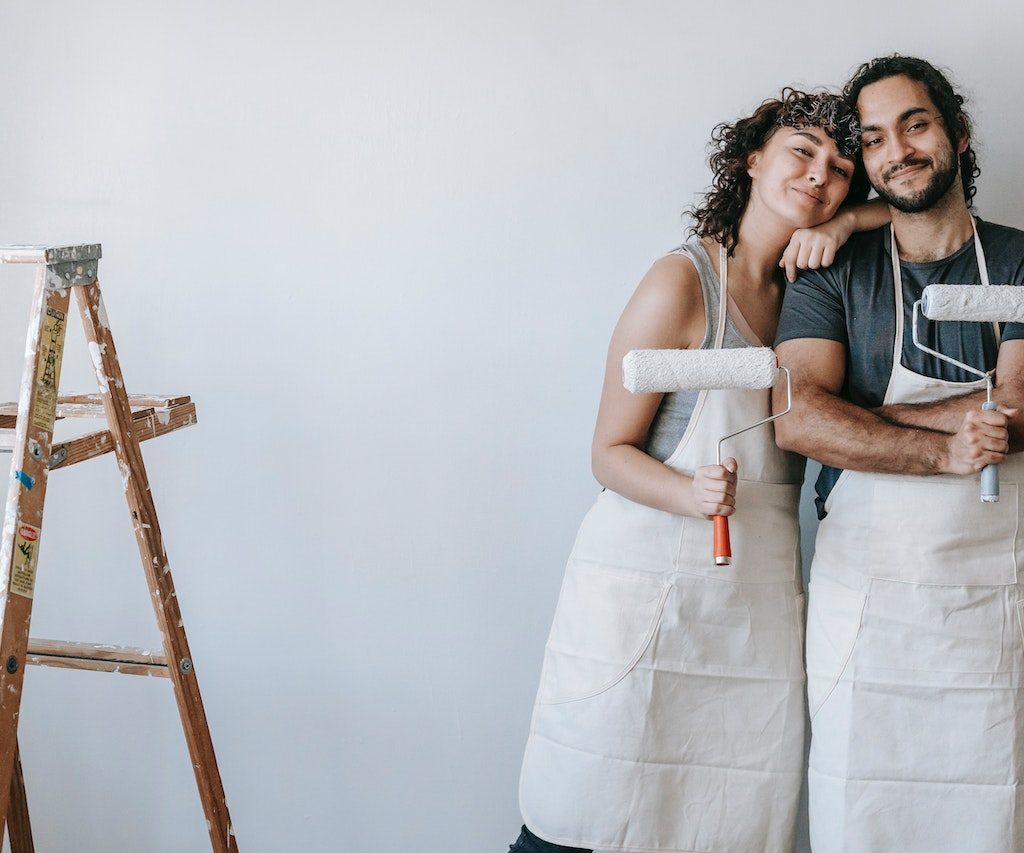 Couple posing with paint rollers in front of painted white wall