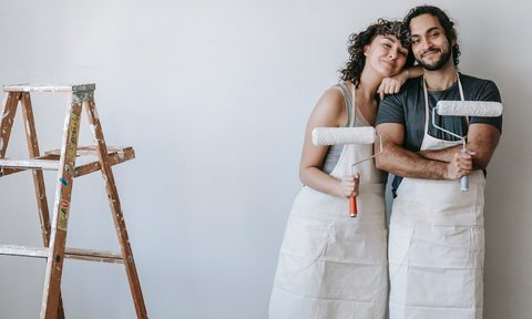 Couple posing with paint rollers in front of painted white wall