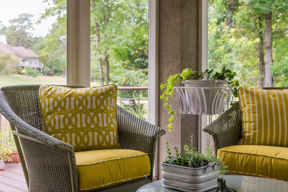 Wicker chairs with bright yellow cushion in screened-in porch