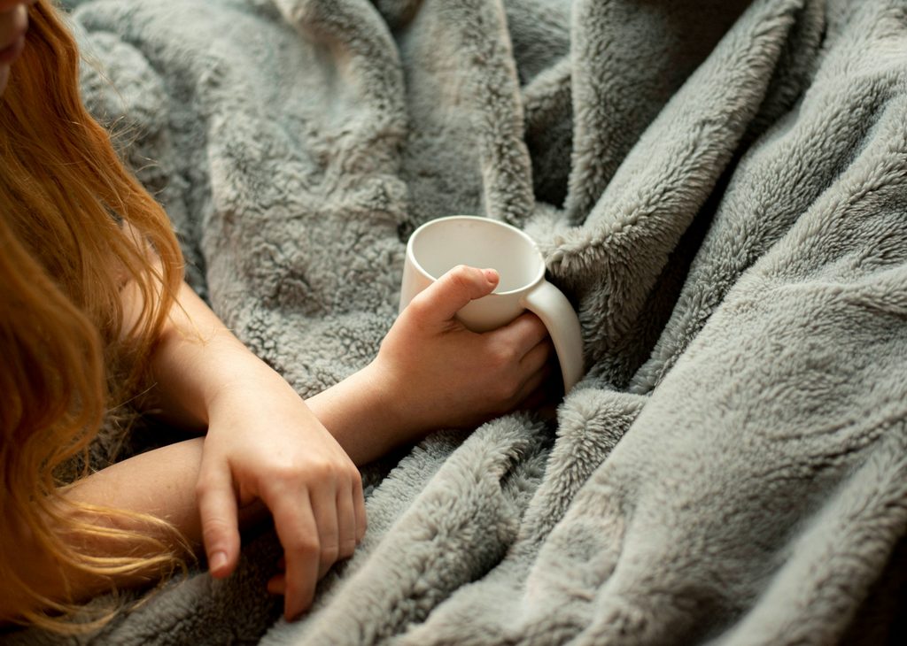 red haired woman holding mug on gray blanket