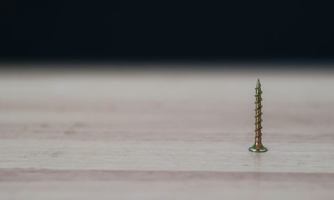 Single screw pointed up on a wood surface