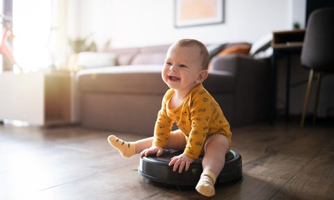 Cute and smiling little baby boy sitting on the robot vacuum cleaner and having a great time.