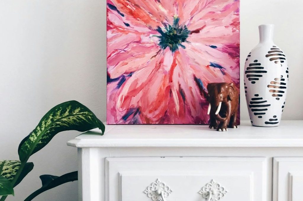 Painting of pink flower on white dresser next to dark green plant