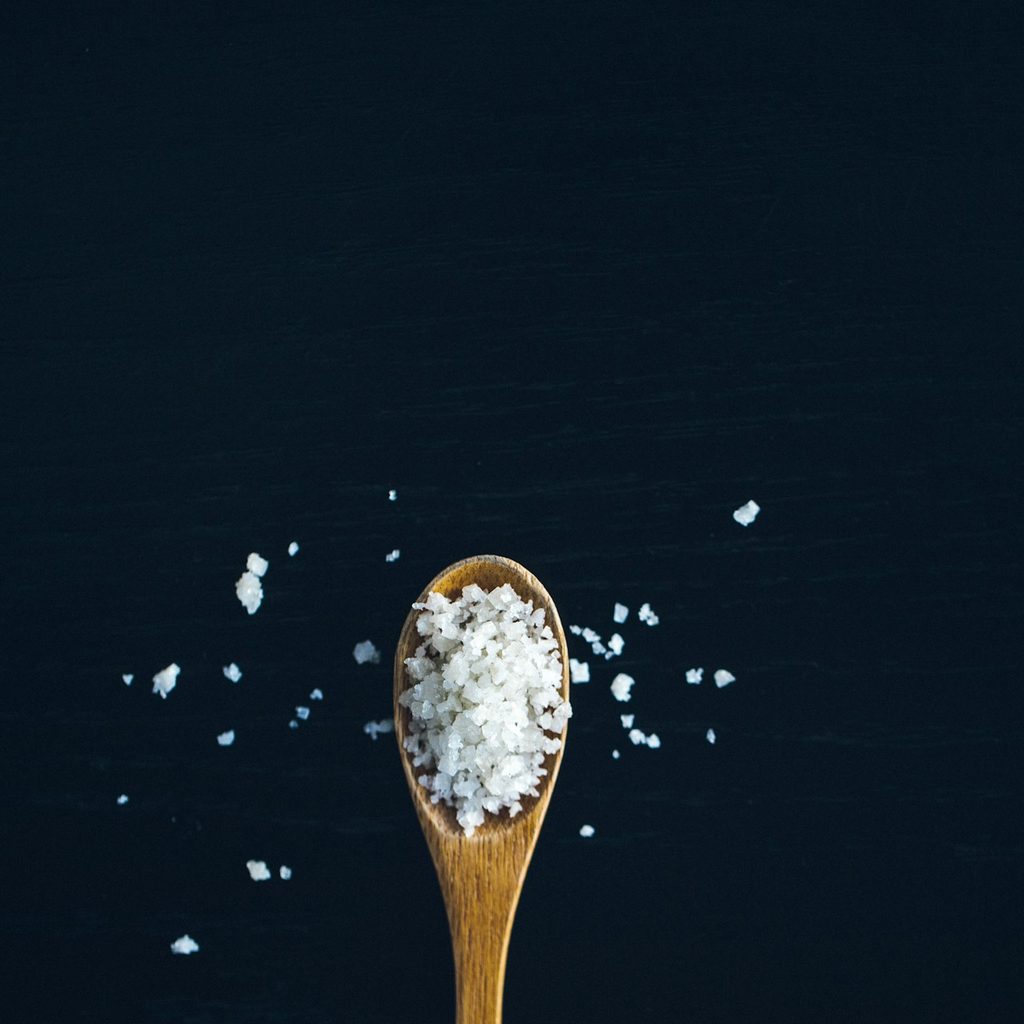 Coarse salt in a wooden spoon on a black surface