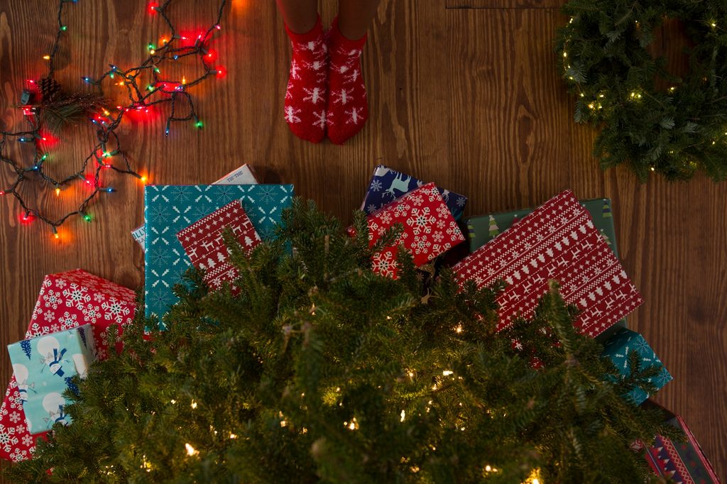 Person in christmas socks standing by lit tree and colored and white christmas lights
