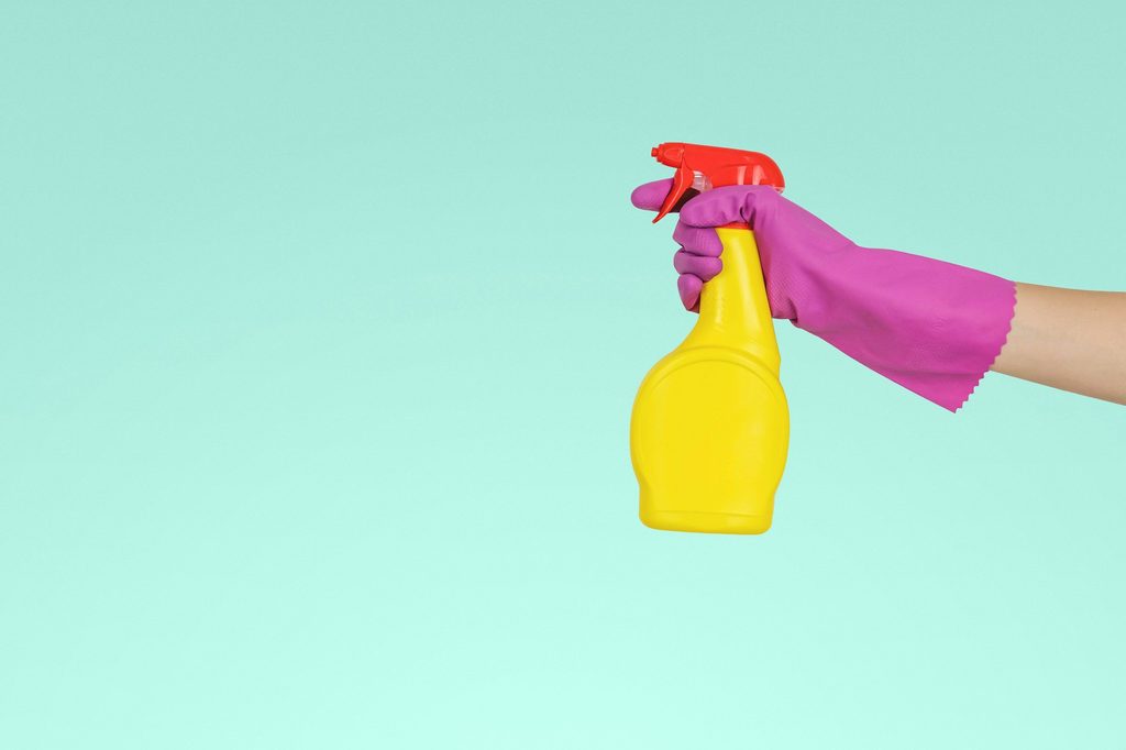 Person in a pink glove holding a yellow spray cleaning bottle.