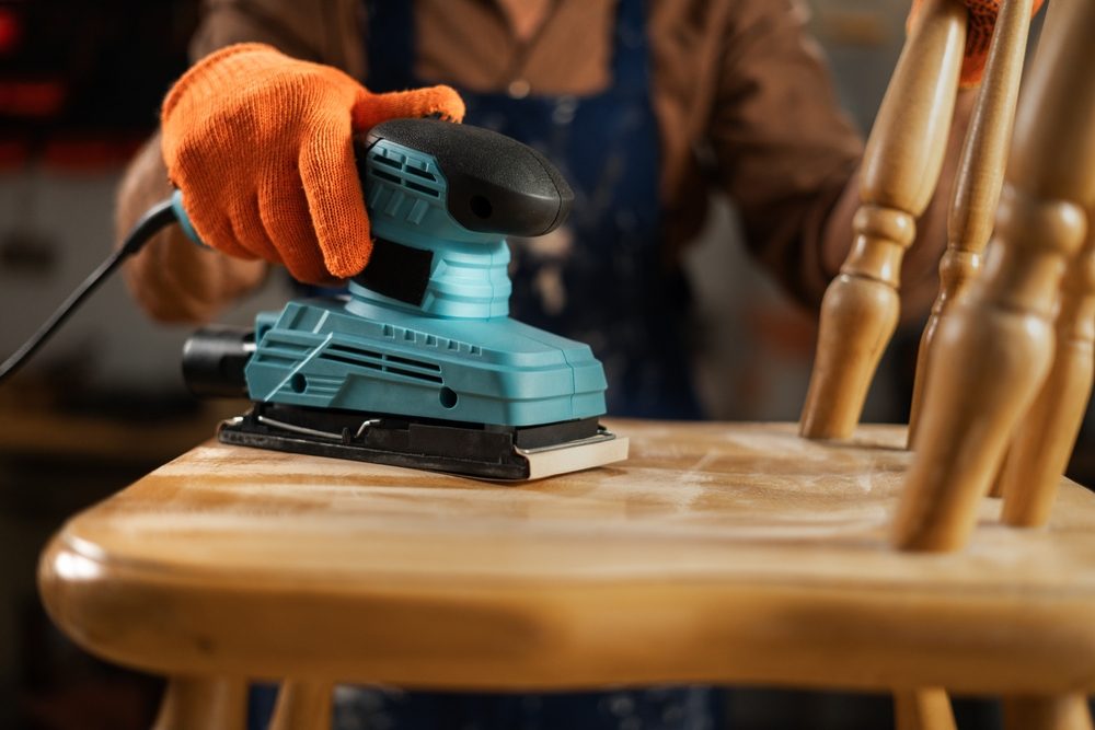 Gloved person using sander on a chair