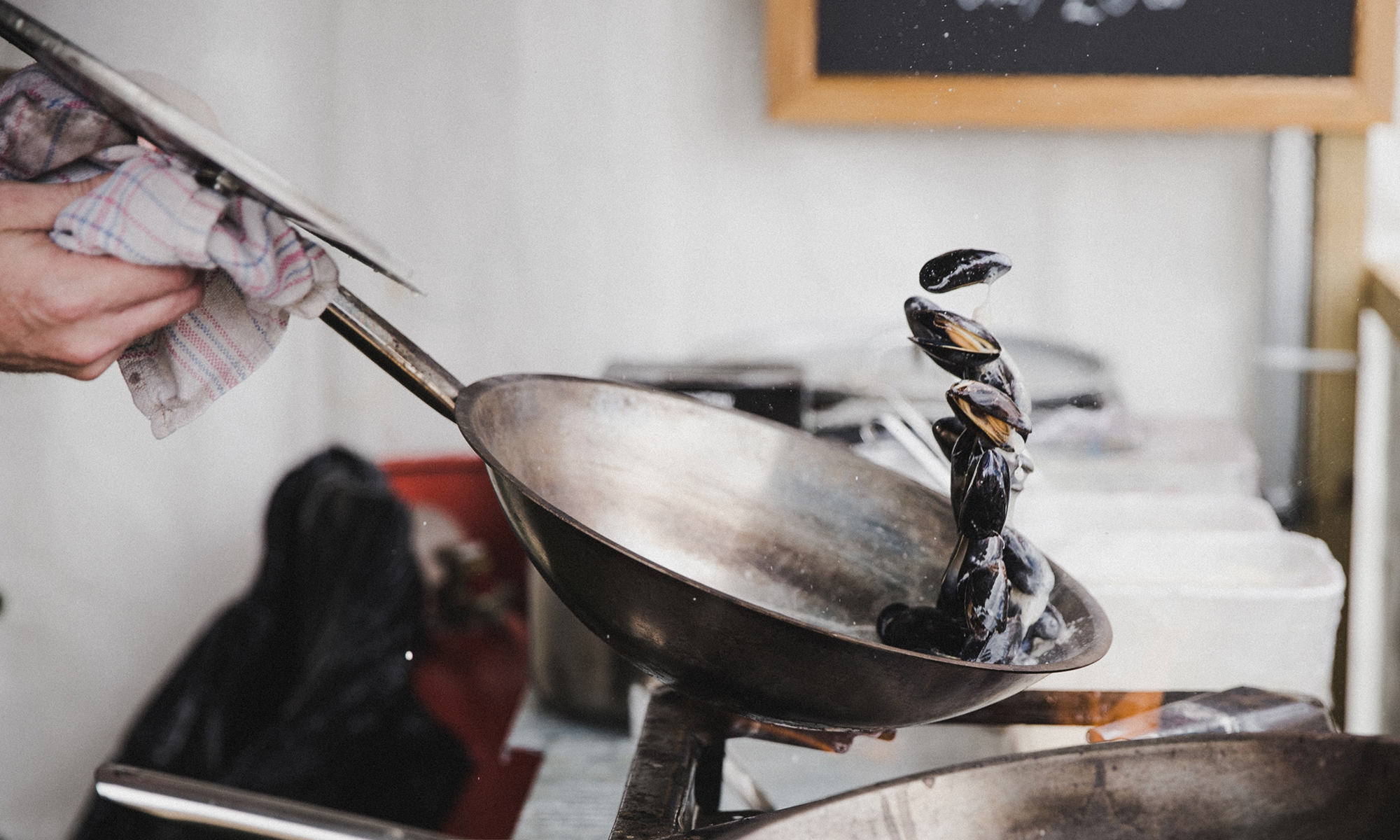 Person tossing clams in stainless steel pan