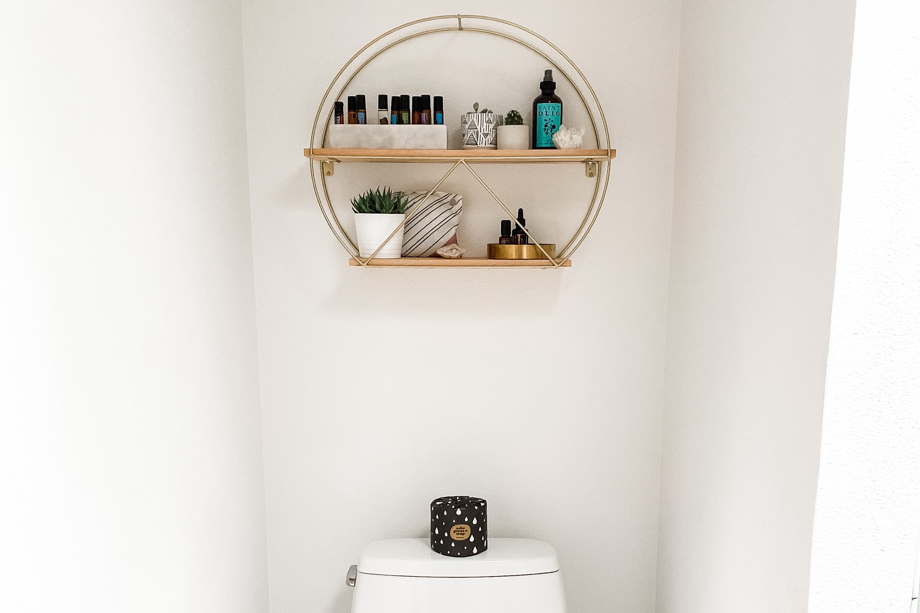 A shelf hanging over a toilet stores bathroom items.