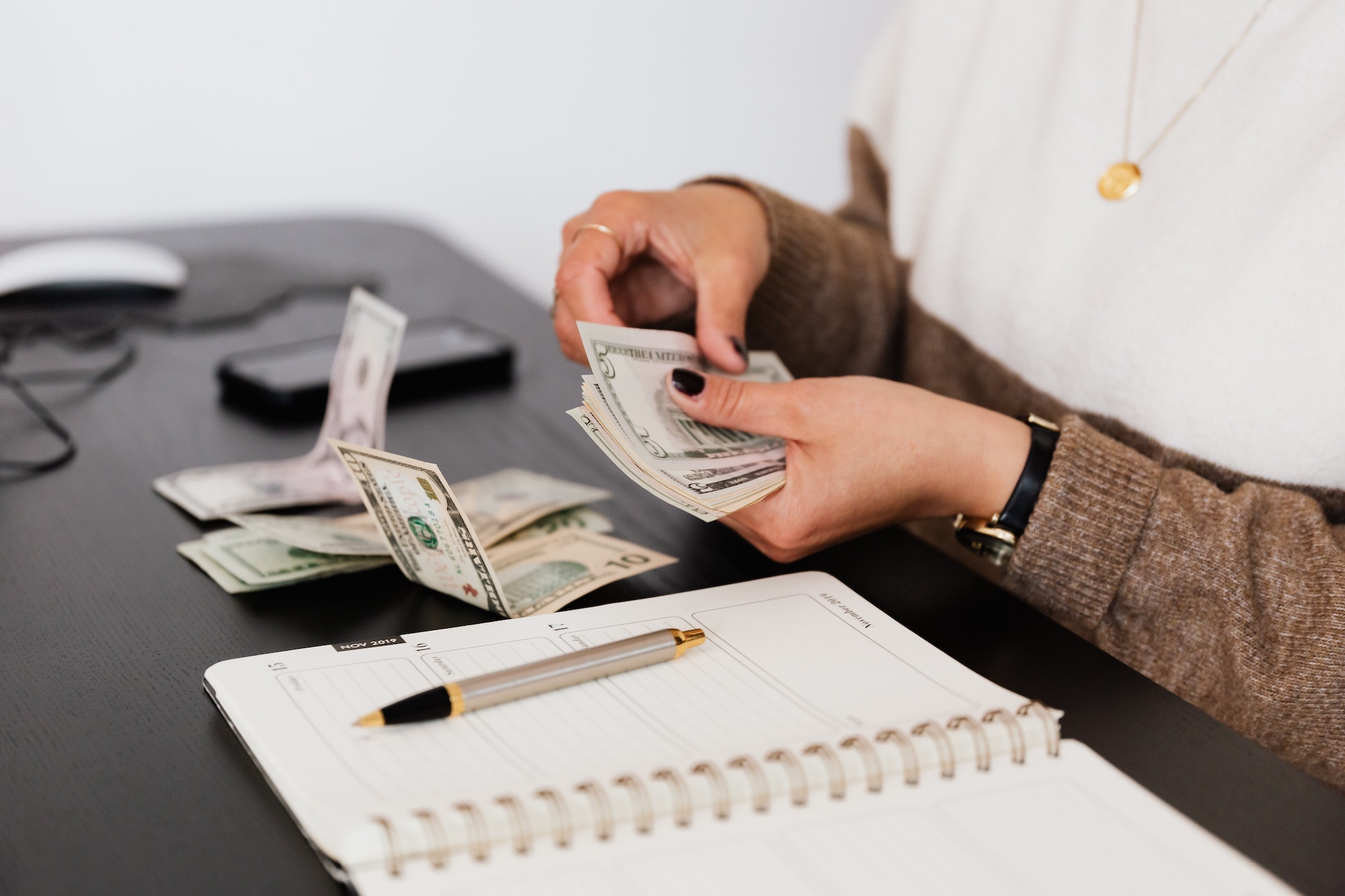 woman counting money next to notebook
