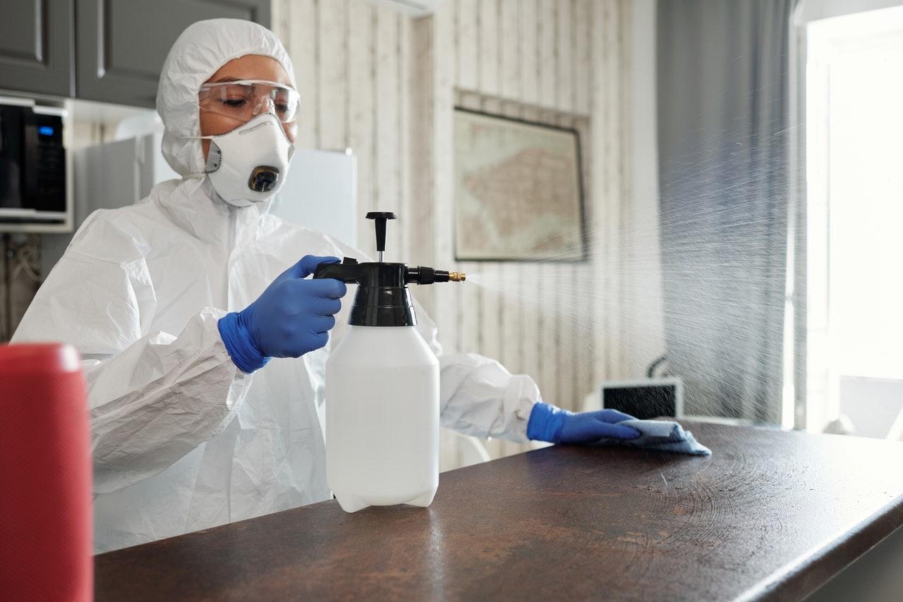 Woman in PPE spraying cleaner on counter