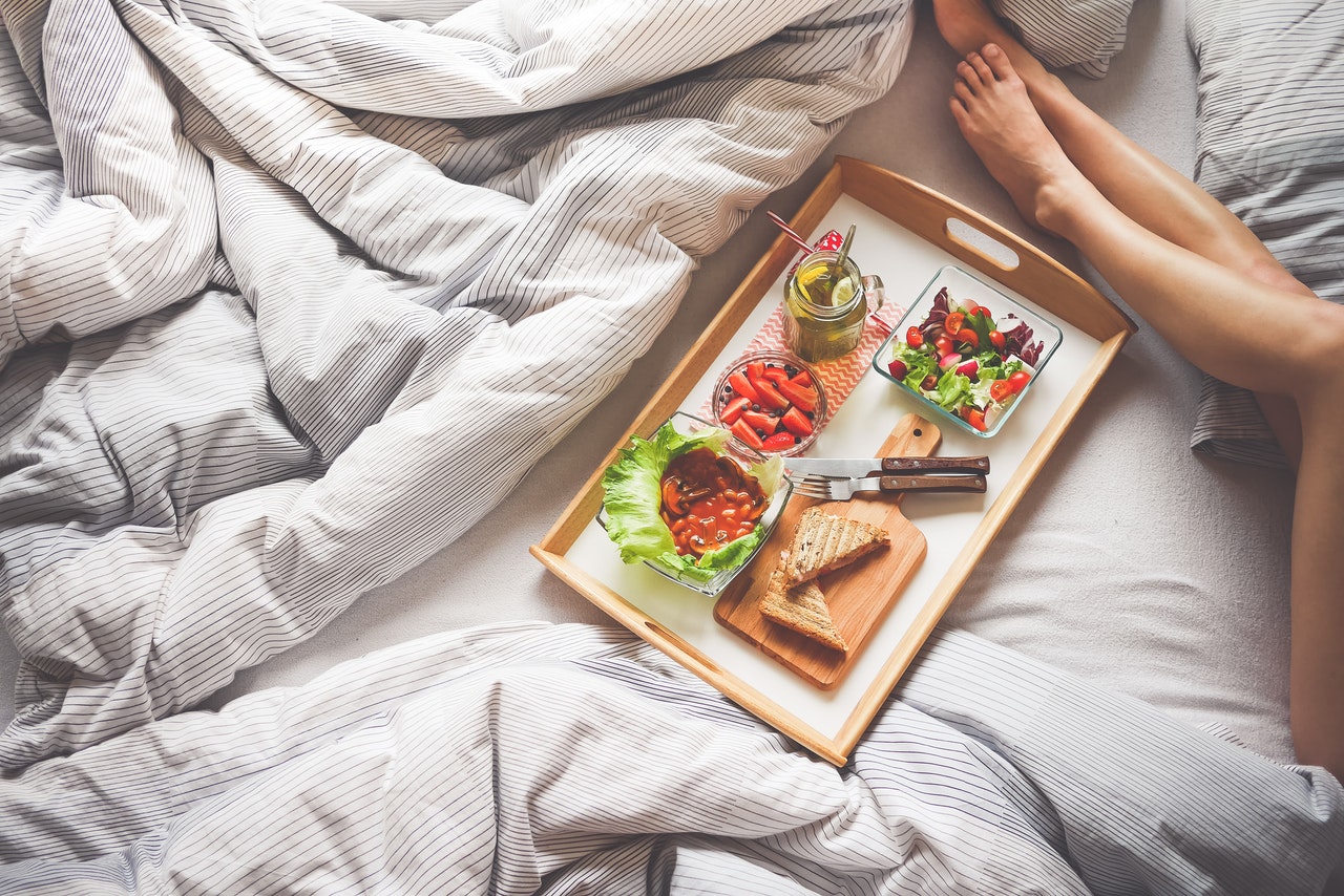 Tray of breakfast food on bed next to woman's legs