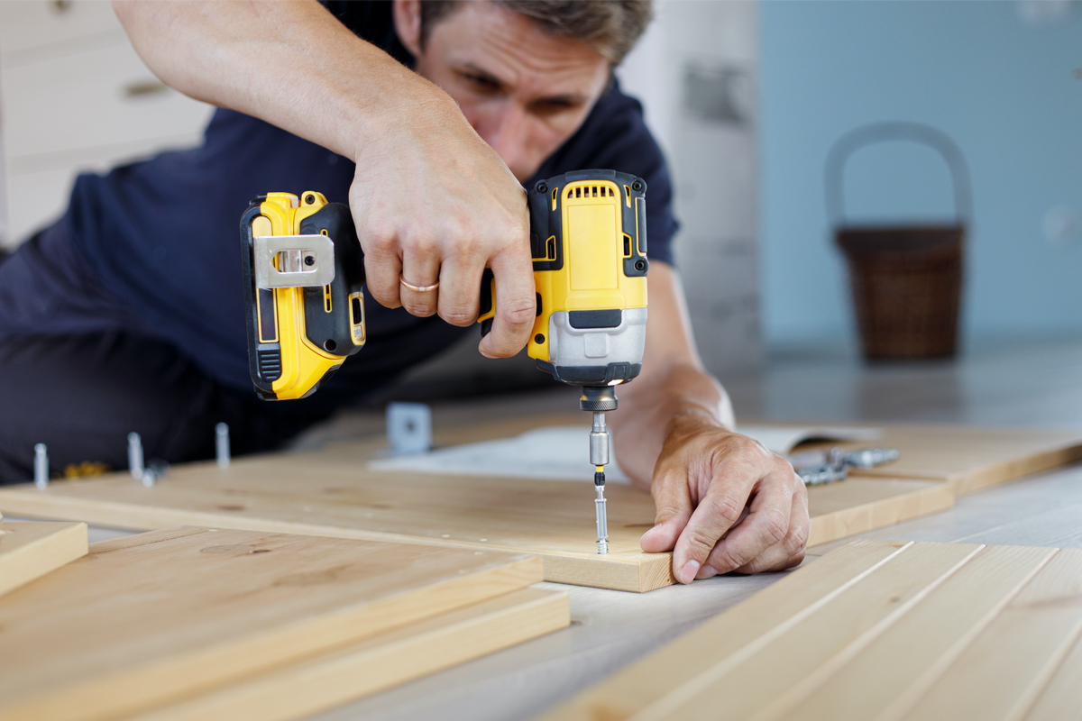 man using an electric drill on a screw in wood