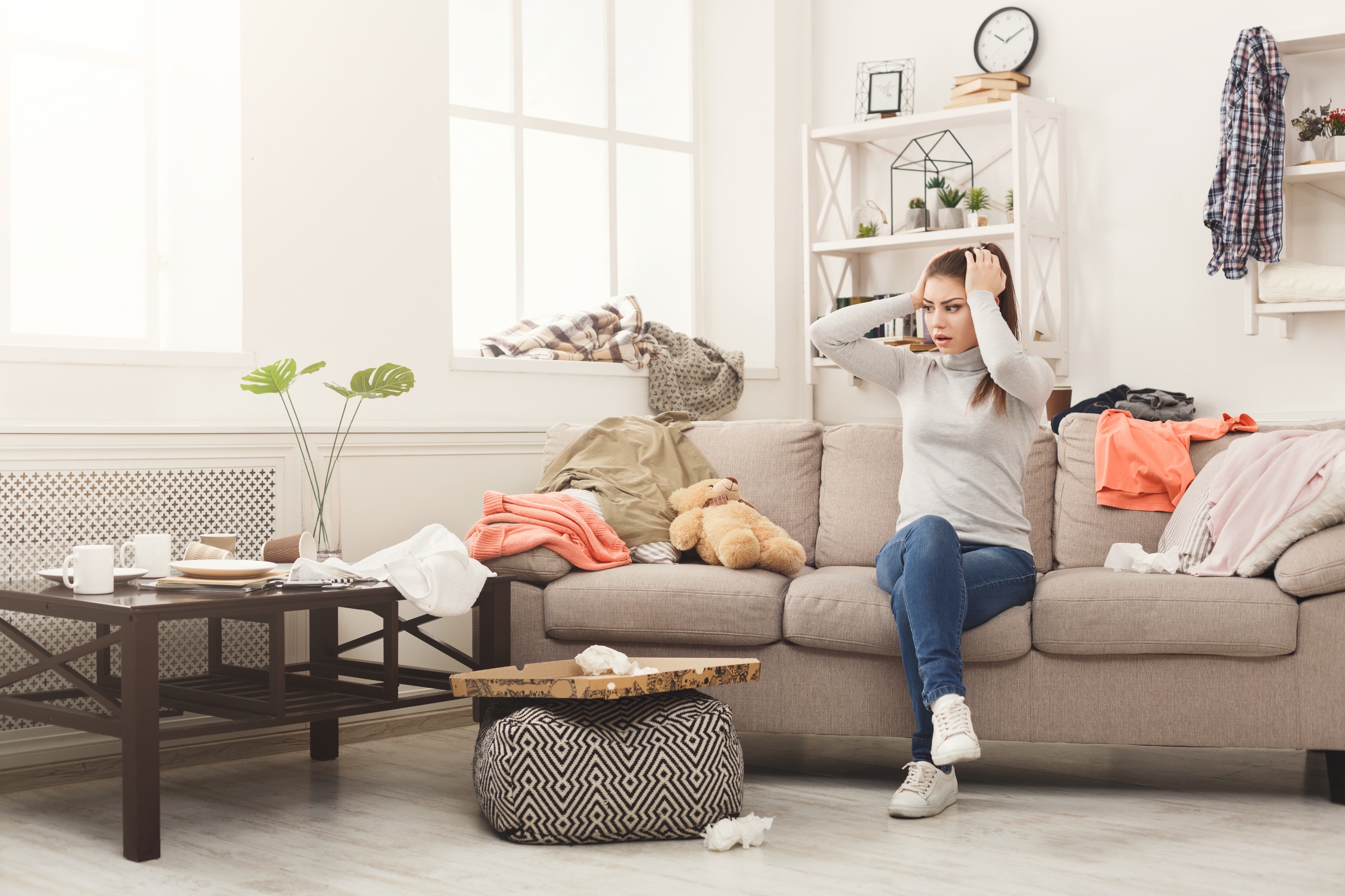 Distressed girl sitting on couch surrounded by clutter.