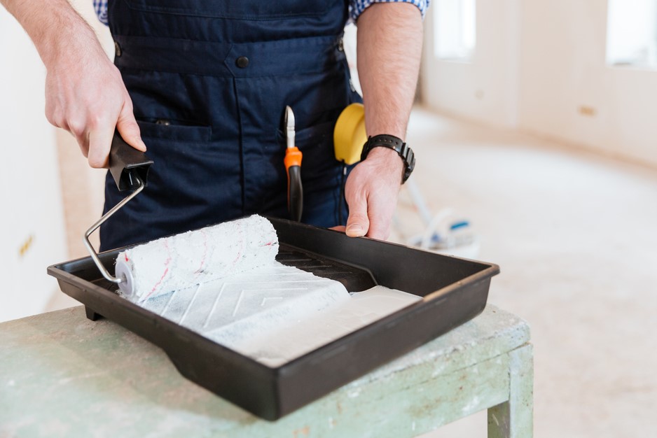 Person using paint roller in tray with white paint