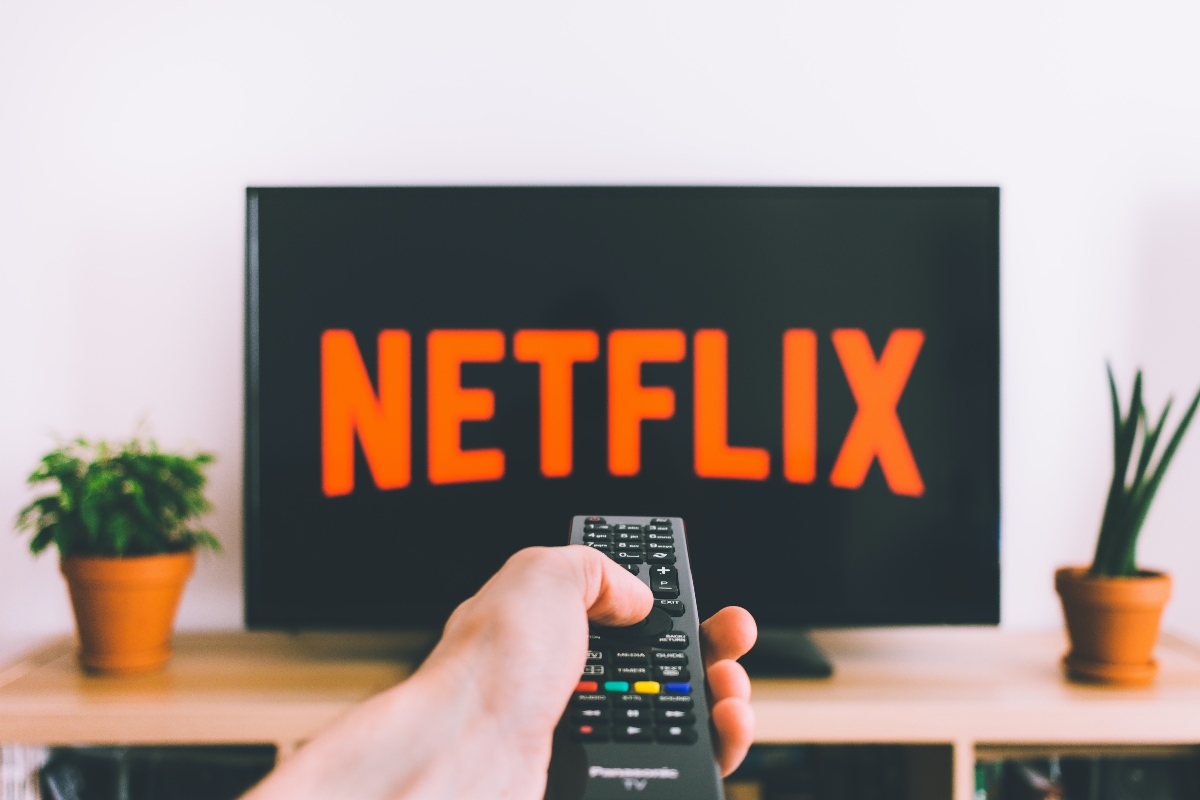 person holding remote towards tv displaying netflix logo