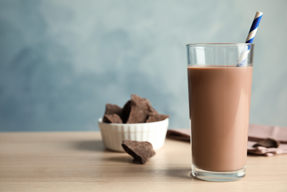 Tall glass of chocolate milk on wooden table near bowl of chocolate