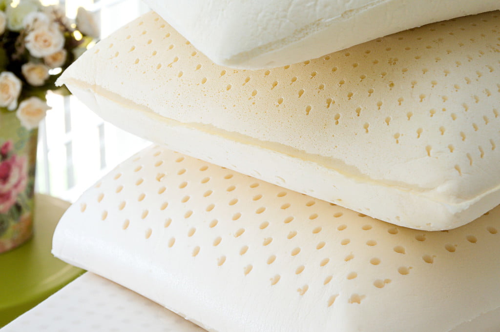 Three natural latex pillows stacked on bed with flowers in background