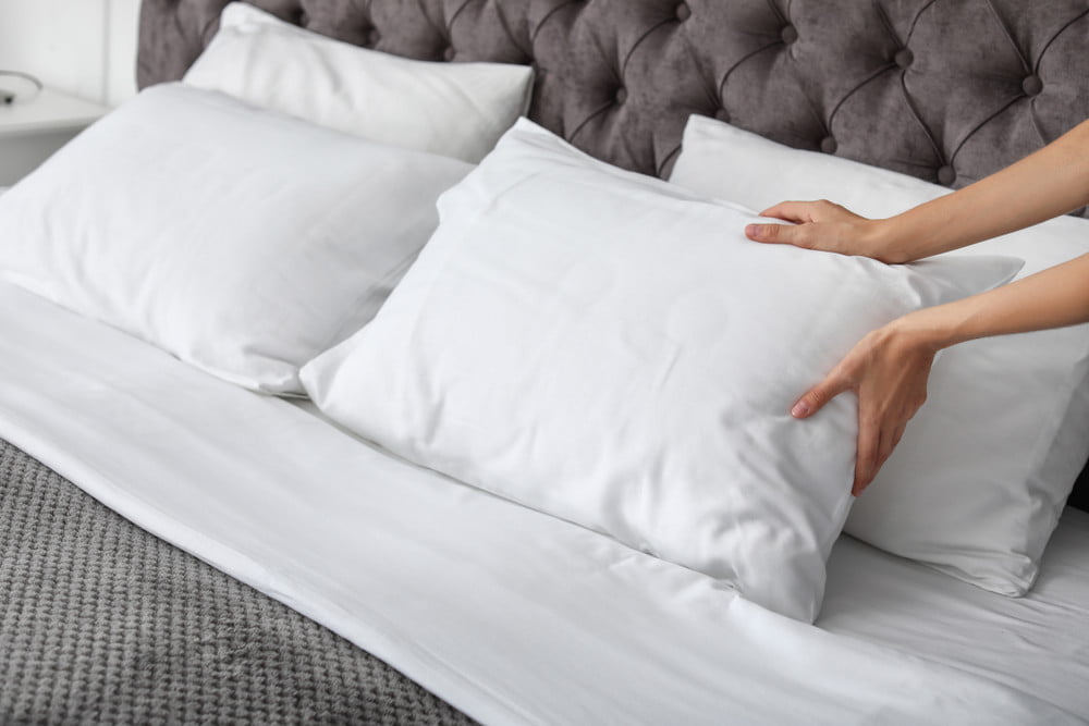 person placing white pillows on bed with gray comforter
