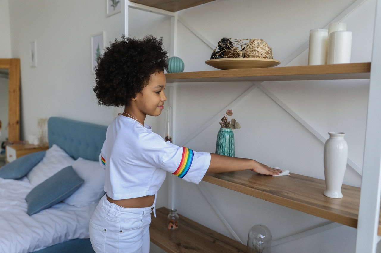 young girl dusting a shelf