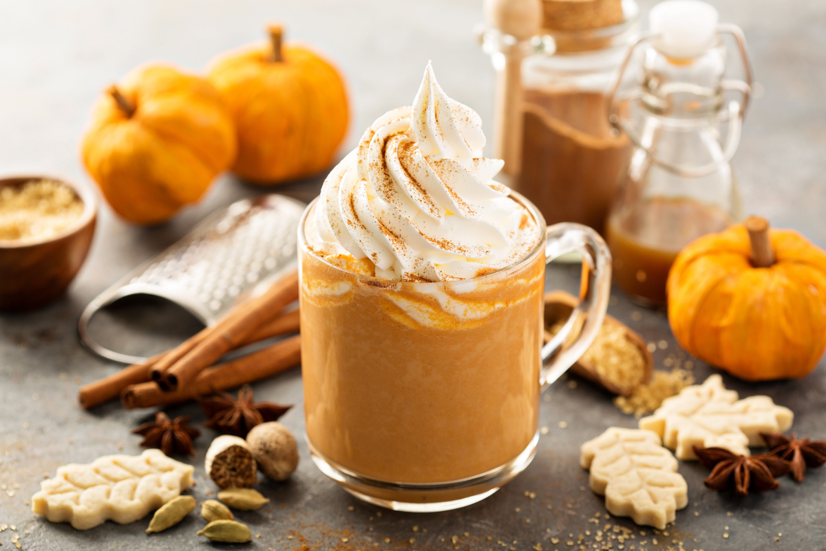 Pumpkin spice latte on a table with pumpkins, cinnamon sticks, and other fall items