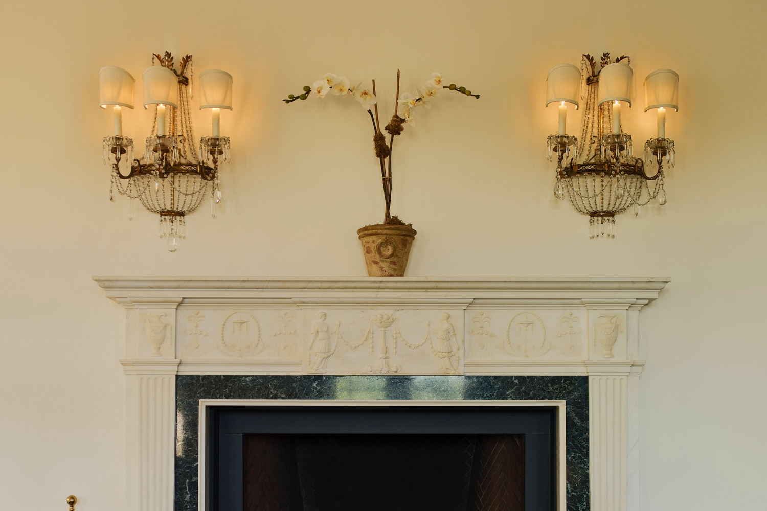 Decluttered mantle with plant and sconces.