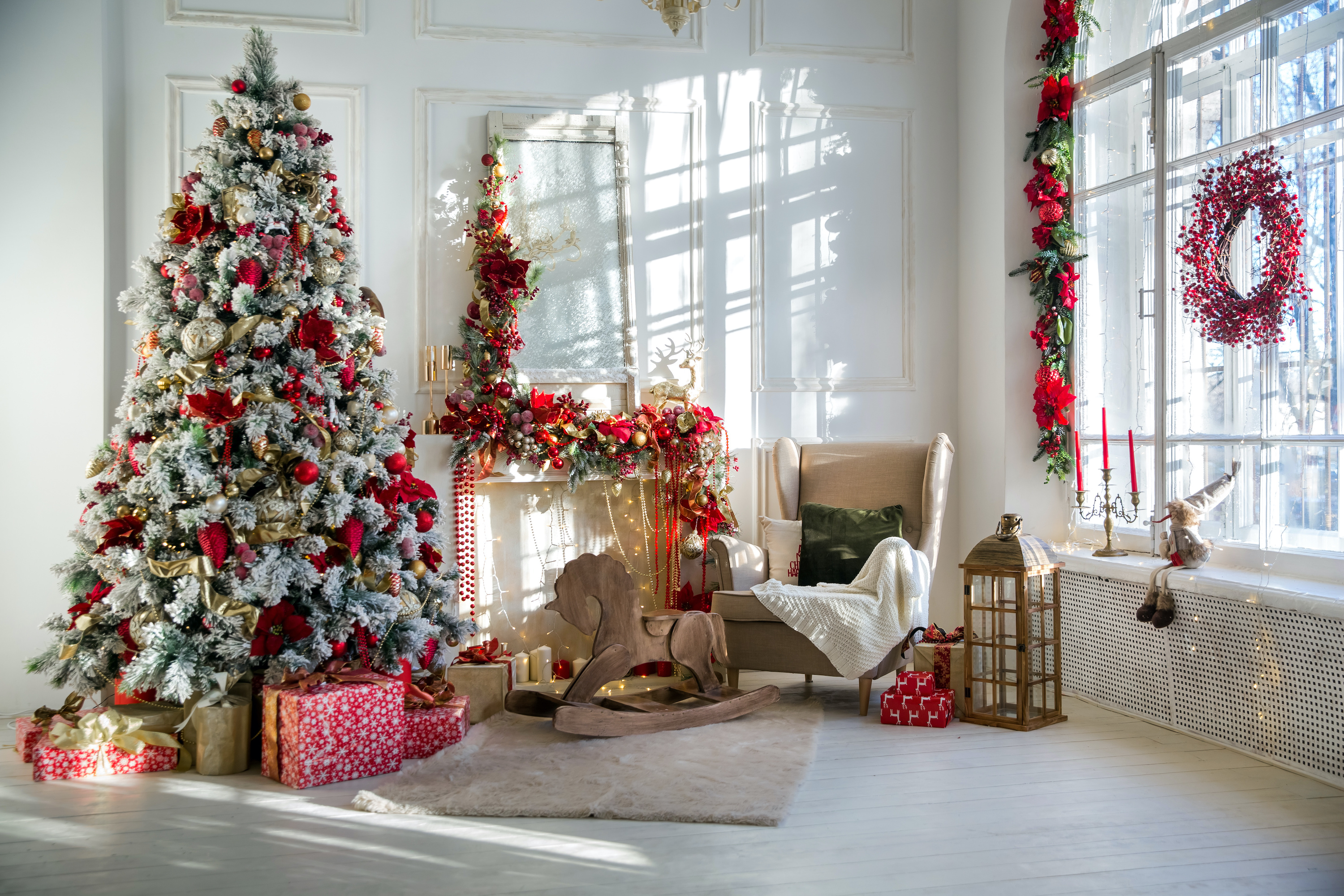 White room interior in red tones with New Year tree decorated, present boxes and artificial fireplace