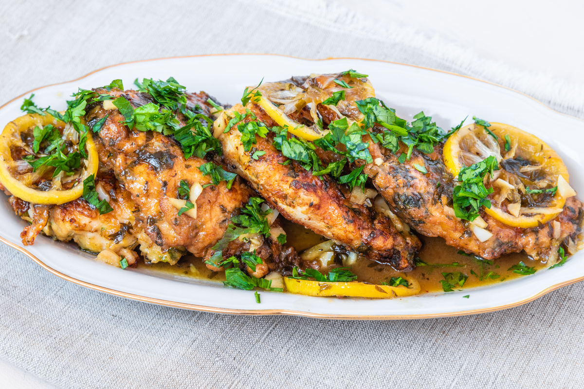 Cooked chicken breasts with lemon and parsley on a white plate