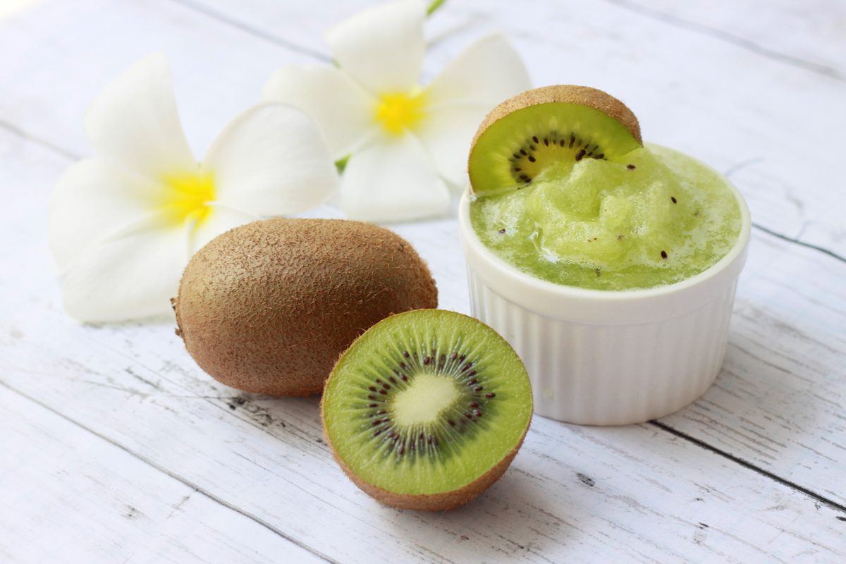 Fresh kiwi fruits sorbet in white bowl with fresh kiwi on wooden background