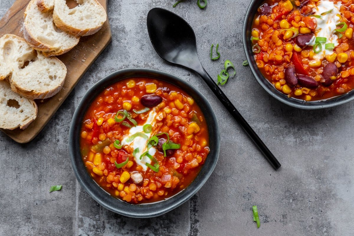 Two bowls of chili with a spoon and bread on a table